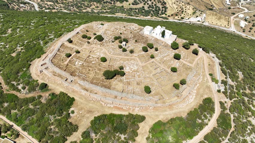 Aerial drone cinematic video of archaeological site of the Mycenaean Citadel and chapel of Agios Andreas built on top of hill overlooking the Aegean sea, Sifnos island, Cyclades, Greece