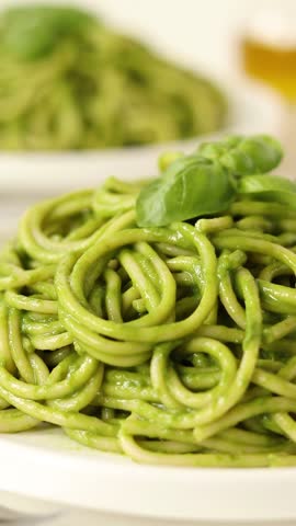 Sprinkling Parmesan cheese on green spaghetti pasta with basil. Vertical video. Close-up. Healthy vegan food preparation.