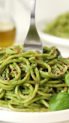Eating green spaghetti pasta with a fork. Vertical video. Close-up. Healthy homemade vegan food.