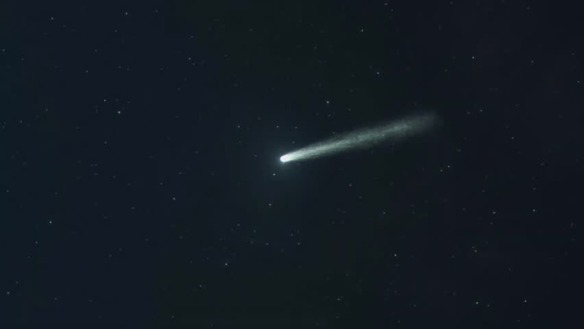 A bright comet with a glowing tail travels through a dark, star-filled night sky.
