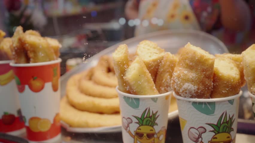 Freshly made churros, sprinkled with sugar, arranged on a tray, ready to be sold at a fair stand, emanating a delicious aroma and golden color.