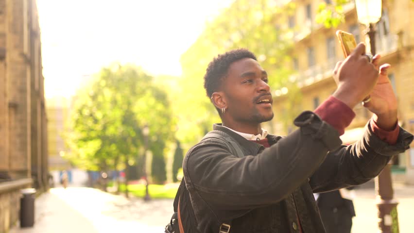 African male young traveler taking photos of a city while walking along the street