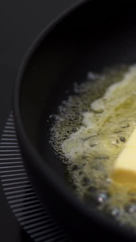 Close up of fresh butter melts and sizzles in hot frying pan on stove. Cooking food. Non-stick pan. Vertical shot