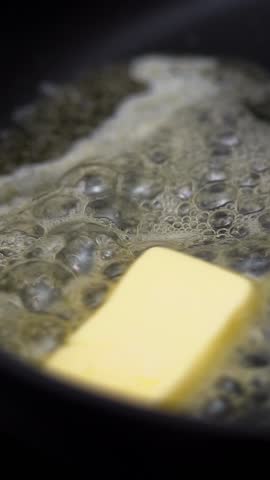 Close up of fresh butter melts and sizzles in hot frying pan on stove. Cooking food. Non-stick pan. Vertical shot