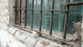 Historic Prison Window with Rusted Iron Bars and Textured Glass at Abandoned Patarei Fortress. Close-up footage reveals the haunting details of original Soviet-era security features - Powered by Shutterstock - Get 15% off with code: PIKWIZARD15
