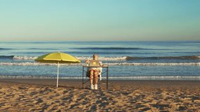 Businesswoman sitting at desk on beach, working on her laptop and talking on her phone. Woman enjoy beautiful weather and ocean view. Drone Shot. - Powered by Shutterstock - Get 15% off with code: PIKWIZARD15