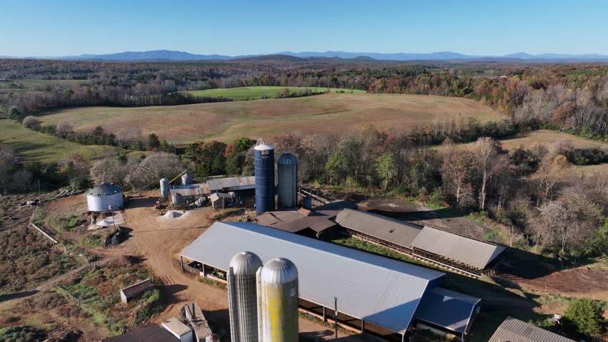 Aerial descend shot of silo storage on farm surrounded by agricultural fields and colored trees in Autumn. American Countryside with blue sky. Wide shot.