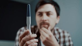 Thoughtful man looks at pregnancy test given by his wife, holding his head in stress. His expression shows disappointment and worry, revealing his unhappiness and reluctance about unexpected pregnancy - Powered by Shutterstock - Get 15% off with code: PIKWIZARD15