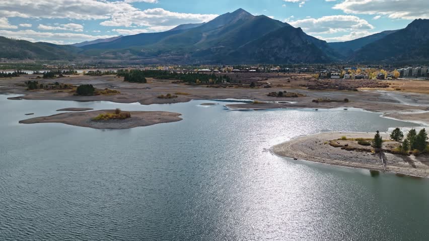 Majestic mountain with rugged terrain overlooking a serene lake and wide landscape, aerial panoramic dolly over Dillon Reservoir Frisco Colorado