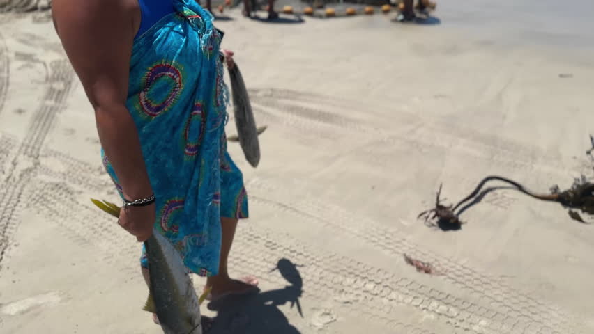 Woman carrying two caught fish on the beach
