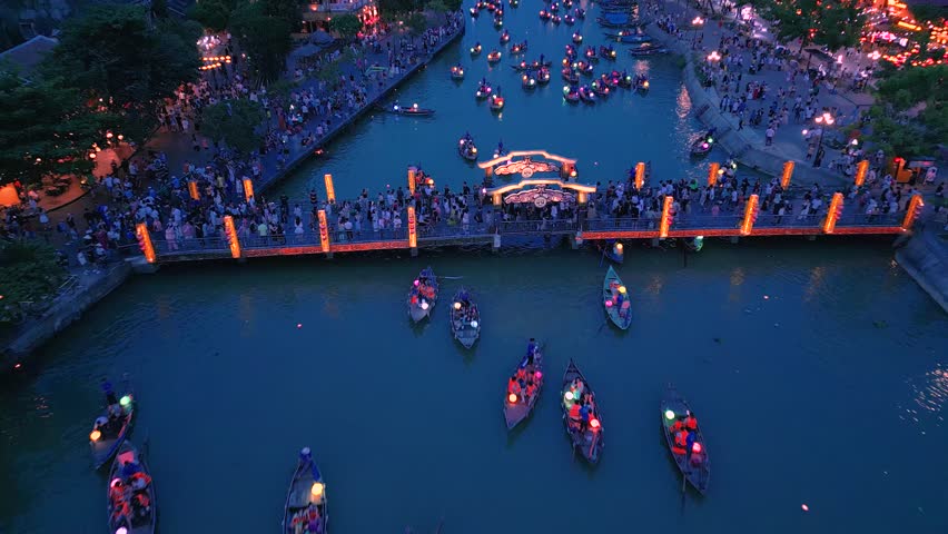 Colorful lanterns illuminate the Bon River as boats glide through Hoi An old city, creating a vibrant nighttime landscape filled with visitors and culture.