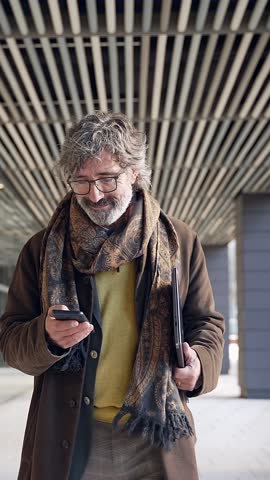 Cheerful Senior Man Walking while Using the Mobile Phone app. Mature Positive Businessman going to work 