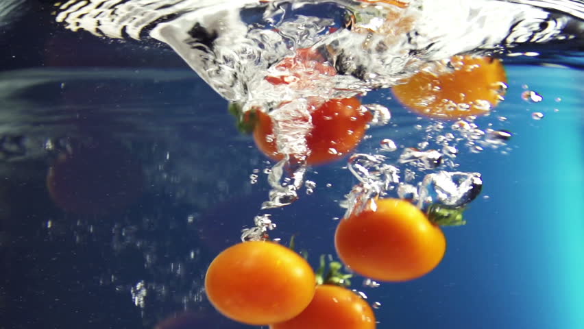 Cherry tomatoes dropped in water vortex on color background
