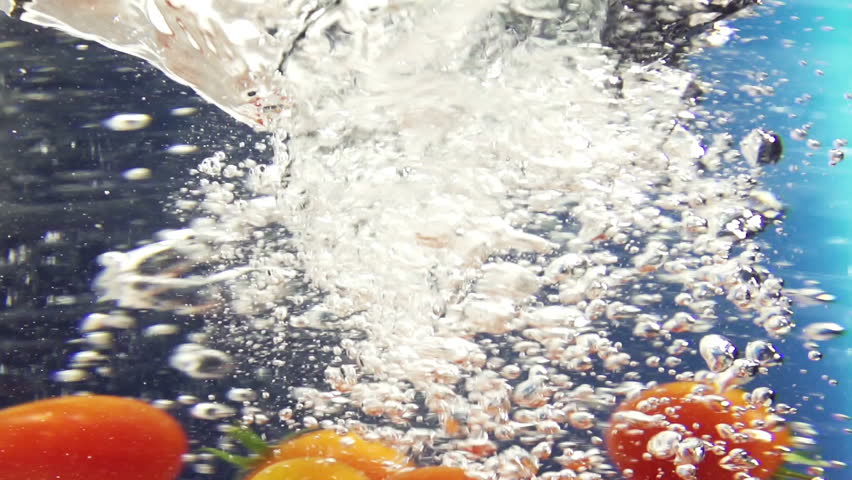 Cherry tomatoes dropped in water vortex on color background