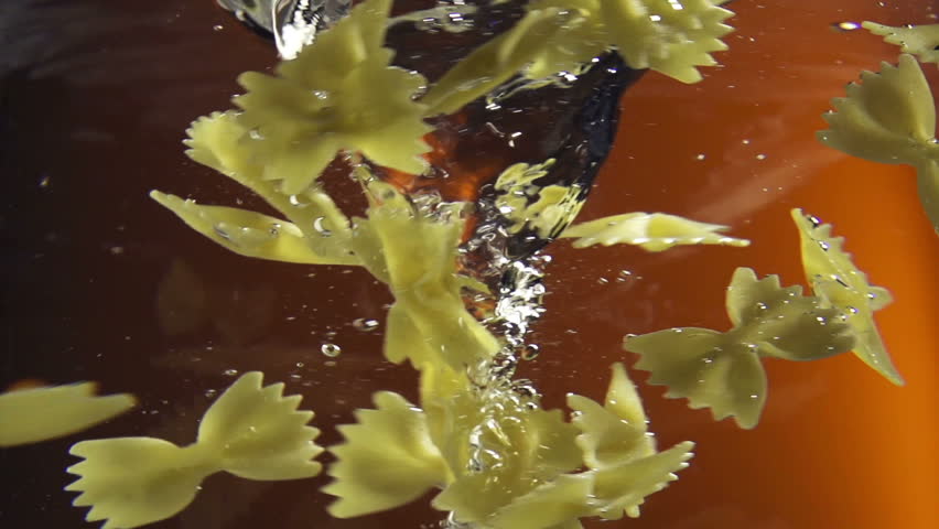 raw farfalle pasta dropped in water vortex on color background