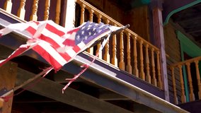 Tattered American flag waving on a rustic wooden porch, symbolizing resilience - Powered by Shutterstock - Get 15% off with code: PIKWIZARD15
