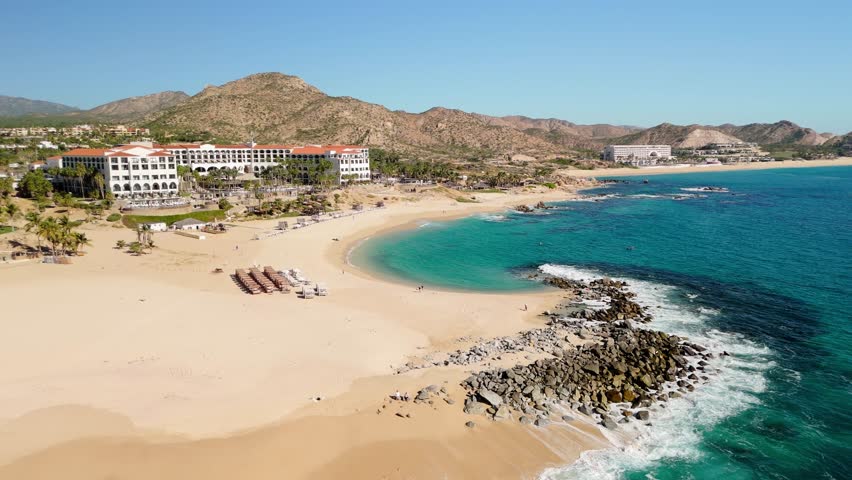 Cabo San Lucas Mexico near San José del Cabo drone view flying around rocks, small waves, and blue sky with no clouds.