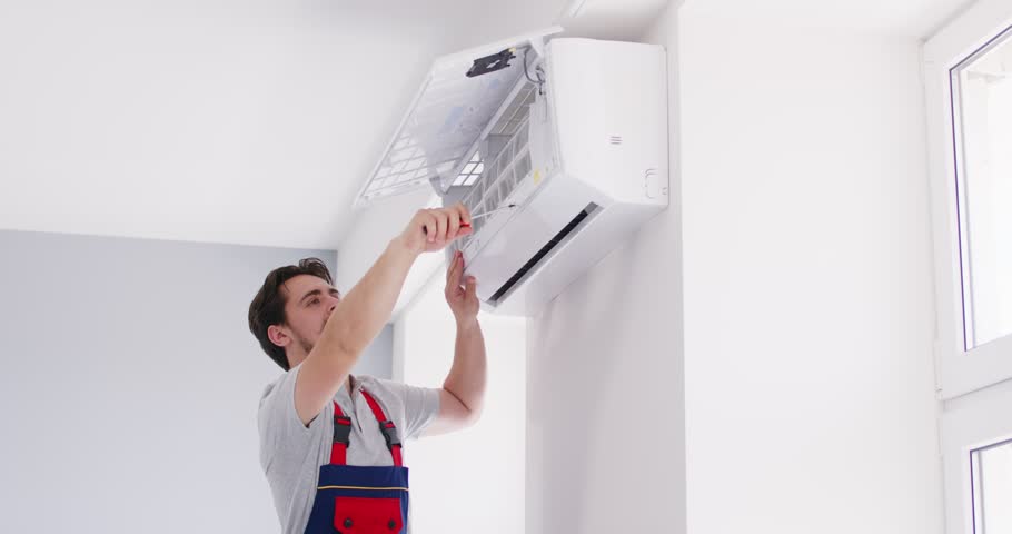 Electrician or technician repairs an air conditioner at home using a screwdriver. The focus is on fixing HVAC issues, maintenance, and the service provided for air conditioning systems.