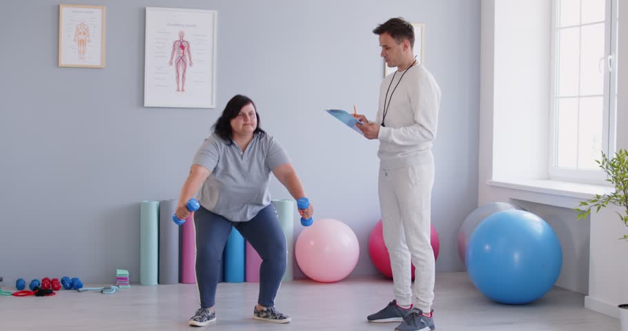 Obese woman doing squats exercise fitness with personal trainer, practice in club, overweight plus size big fat fit lady weight loss, improving body, effective exercise program for slimming, health