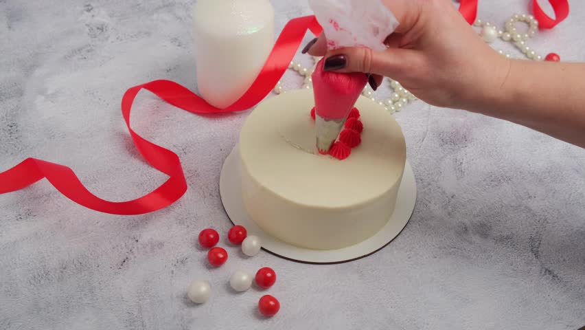 A pastry chef decorates a cake with red heart-shaped cream for Valentine