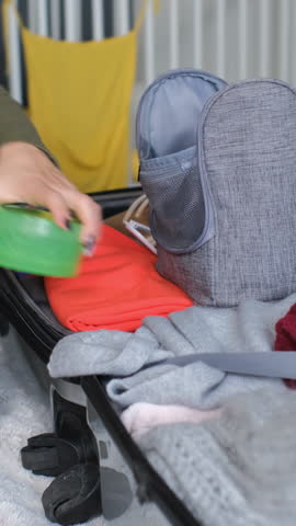 Vertical video. Close-up of a female packing a travel bag with cosmetics and essentials, ensuring everything fits into her suitcase for a trip