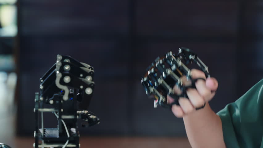 Asian teenage boy joyfully tests a robot hand and arm exploring technology in a technical college. Embracing AI humanity and innovation for educational development.