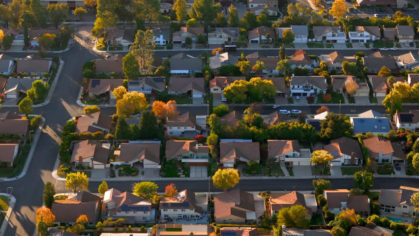 An enchanting aerial view unveils a picturesque suburban neighborhood that beautifully showcases serene residential homes bathed in the warm glow of a breathtaking sunset over Los Angeles