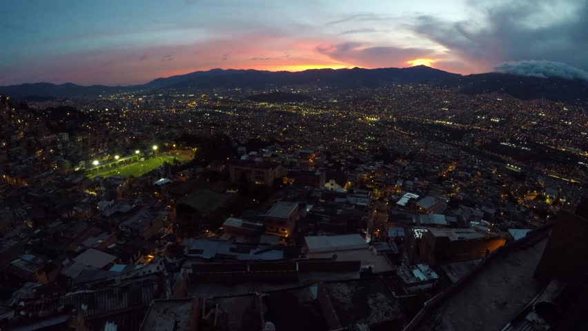 Street lights illuminate favelas and a soccer field in a valley in the mountains at dusk in the city of Medellin, Colombia
