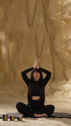 Vertical video of woman practices meditation, sits cross-legged in sand cave in desert dune, representing clearing mind, copy space. Feels inner harmony and balance, improves self-awareness