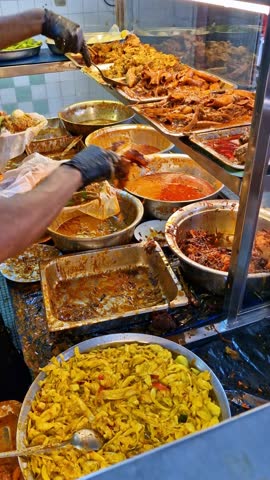 Vertical footage of unidentified worker prepares 'nasi kandar' or 'kandar' rice in Penang, Malaysia. 'Nasi kandar' is a popular spicy dish originating from Penang Indian Muslim traders