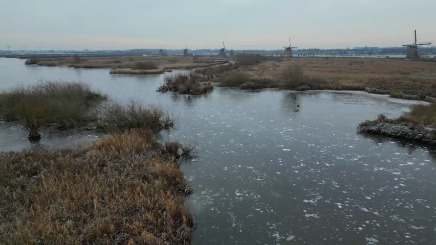 The famous Kinderdijk windmills in the Netherlands covered in frozen snow seen from drone. The national museum and UNESCO heritage in the winter season. Extreme cold phenomenon in the Dutch lands 4k