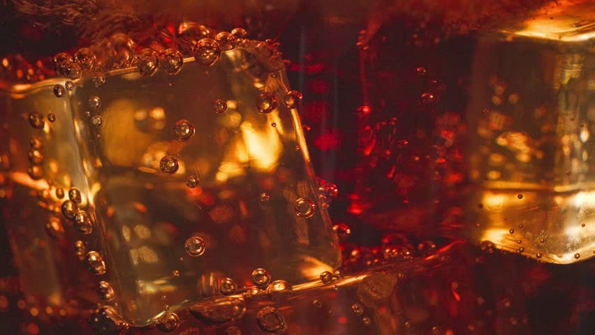 fresh cola pouring into glass with ice, close up. bubbles move around ice cubes macro