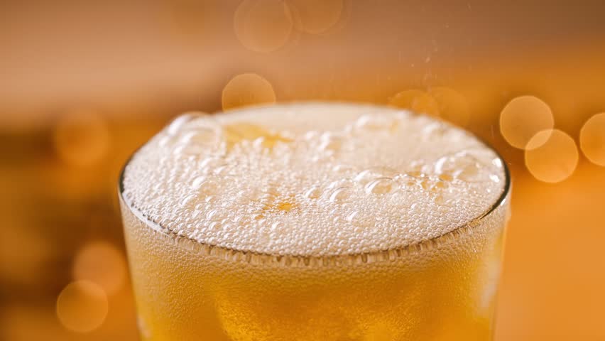 fresh sparkling orange drink pouring into glass with ice, close up. Defocused orange festive background