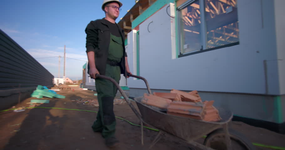 Man pushing a wheelbarrow loaded with wooden materials on a construction site, working on building project, outdoor construction, teamwork, focus on manual labor
