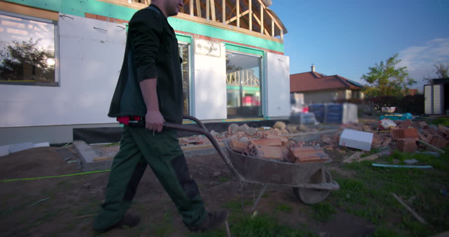 Man pushing a wheelbarrow loaded with wooden materials on a construction site, working on building project, outdoor construction, teamwork, focus on manual labor