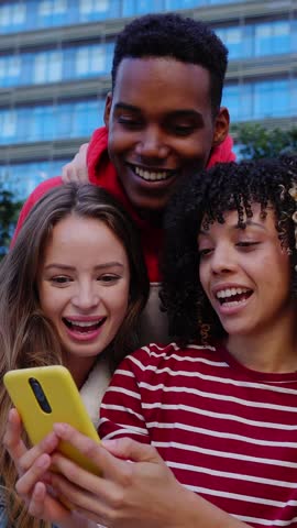 Vertical HD video of young multiracial group of teenage student friends watching social media content on mobile phone app at city street. Youth and technology lifestyle concept