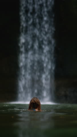 Portrait: young girl posing at a waterfall posing. Beautiful woman stands in the water of a river on island Bali, Indonesia. Sexy female has wet hair. Travel tourism, vacation concept. wild nature