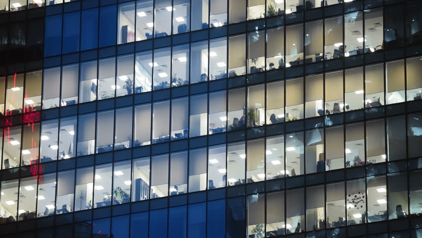 Modern tall glass building panoramic windows. Financial business center. Skyscraper facade background. Busy people work late office district. High downtown tower night view. Evening light. City life.