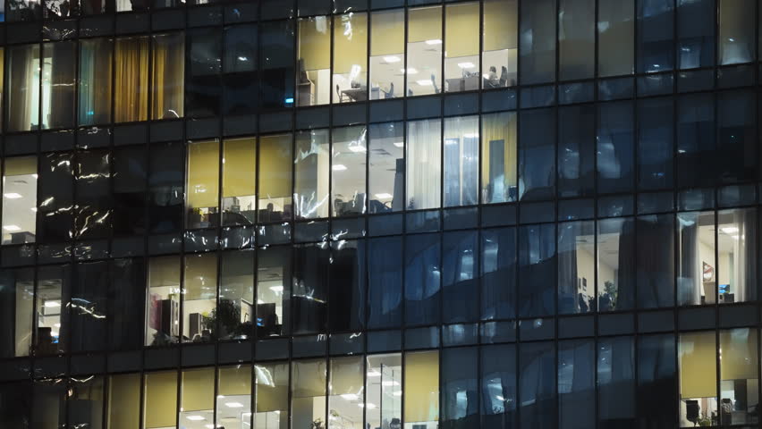 Modern tall glass building panoramic windows. Financial business center. Skyscraper facade background. Busy people work late office district. High downtown tower night view. Evening light. City life.