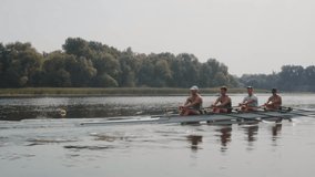 Rowing team training. Side view of 4 young caucasian male rowers, during a rowing practice, athlete sitting in a boat in the river Dnipro, rows through a calm water in autumn. 4k footage. City area in - Powered by Shutterstock - Get 15% off with code: PIKWIZARD15