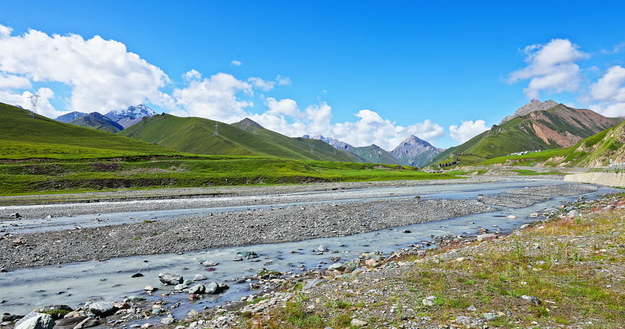 Flowing river and green grassland with mountain natural landscape in summer. Beautiful scenery along the Duku Highway in Xinjiang, China.