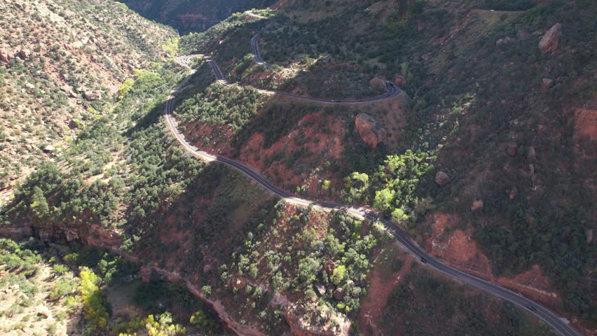 Flying through a stunning desert valley, the camera follows winding roads before panning up to reveal towering cliffs and vast landscapes in Zion National Park.
