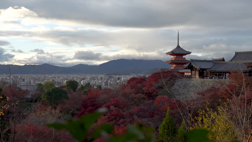 Kiyomizu-dera pagoda in Kyoto amid fall foliage under cloudy sky