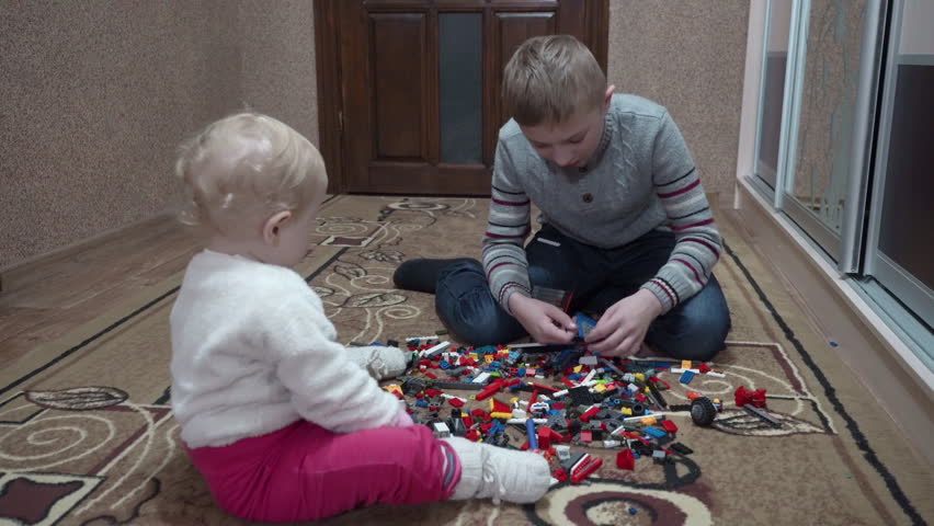 boy with little sister playing with toys, an older brother and his younger sister play and build a constructor from colored blocks, two children play in the room