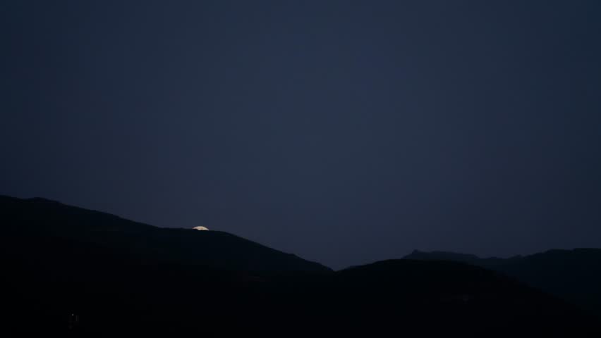 Full Moon Rising Over Mountains Through Clouds