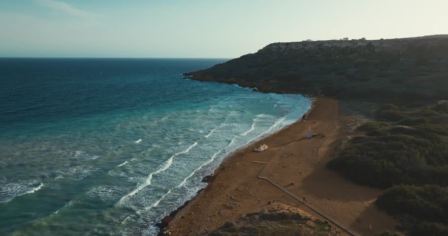 Aerial view of Ramla beach on the island of Gozo, Malta. The waves of the Mediterranean Sea crash on the sand at sunset in a beautiful seascape of nature. High quality 4k footage