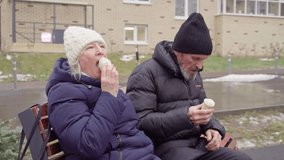 Elderly couple in warm winter clothing sitting on a bench, enjoying ice cream cones outdoors on a cold day. Retirement life concept - Powered by Shutterstock - Get 15% off with code: PIKWIZARD15