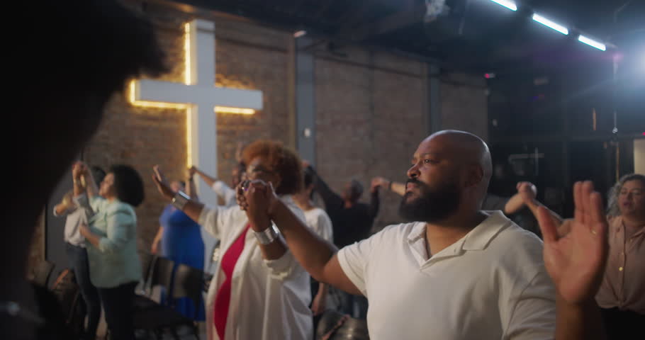 Congregation holding hands during worship, standing in unity and faith, illuminated cross in the background symbolizing community and spiritual connection