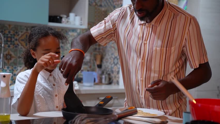 African American father man hand frying pancakes together with daughter. Family daily routine, common habits, healthy food cooking for dinner, dad and child active lifestyle