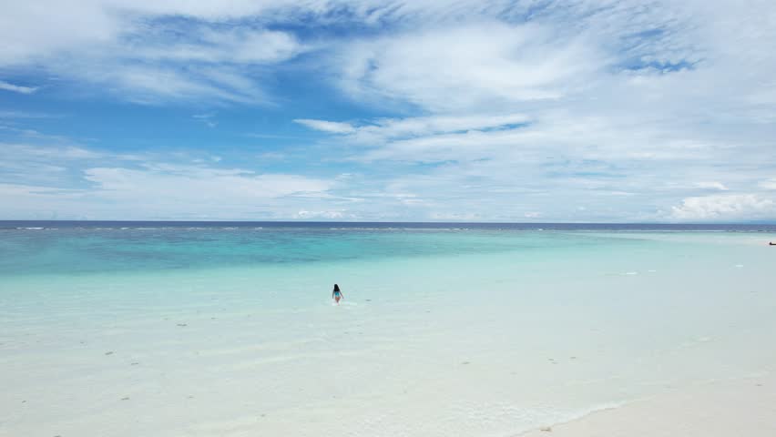 Girl swimming into the ocean in a Mantigue island in Camiguin, Philippines. Turquoise and a cristal clear water, bue sky and exotic landscape 